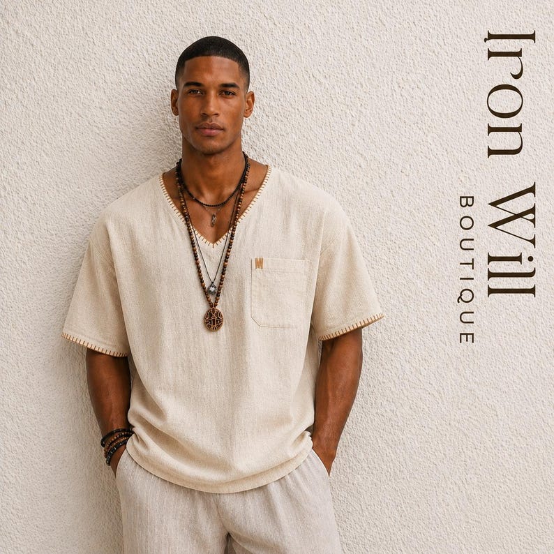 May include: A beige V-neck short-sleeve shirt with a pocket and decorative stitching. The shirt is paired with matching pants and layered necklaces. The text "Iron Will Boutique" is visible on the right side.