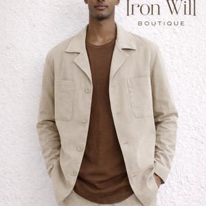 Peut inclure: Un homme porte une veste en lin beige et un pantalon assorti sur un t-shirt marron. La veste a des boutons et des poches. Le texte "Iron Will BOUTIQUE" est visible en haut à droite.