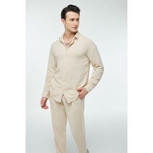 May include: A light beige long-sleeved shirt with a button-up front and a matching pair of pants.