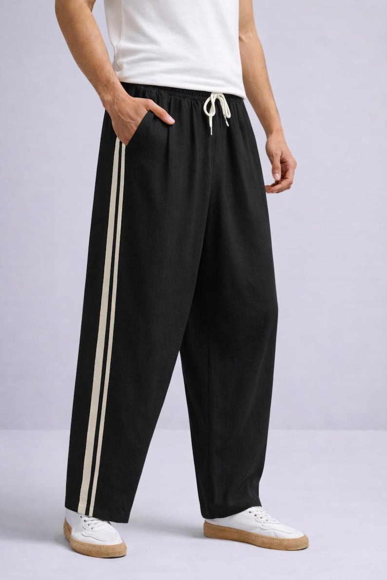 Puede incluir: Pantalones negros de pernera ancha con dos rayas verticales de color crema en el lateral. Los pantalones tienen cintura con cord&oacute;n y se combinan con zapatillas blancas. El modelo lleva una camiseta blanca.