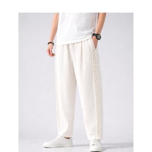 May include: Off-white linen pants with a drawstring waist and decorative lace trim down the sides. The pants are loose-fitting and paired with white sneakers and a white t-shirt. The overall style is casual and comfortable.