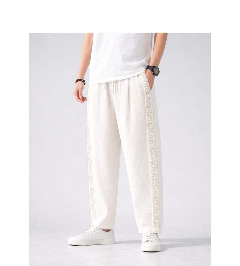 May include: Off-white linen pants with a drawstring waist and decorative lace trim down the sides. The pants are loose-fitting and paired with white sneakers and a white t-shirt. The overall style is casual and comfortable.