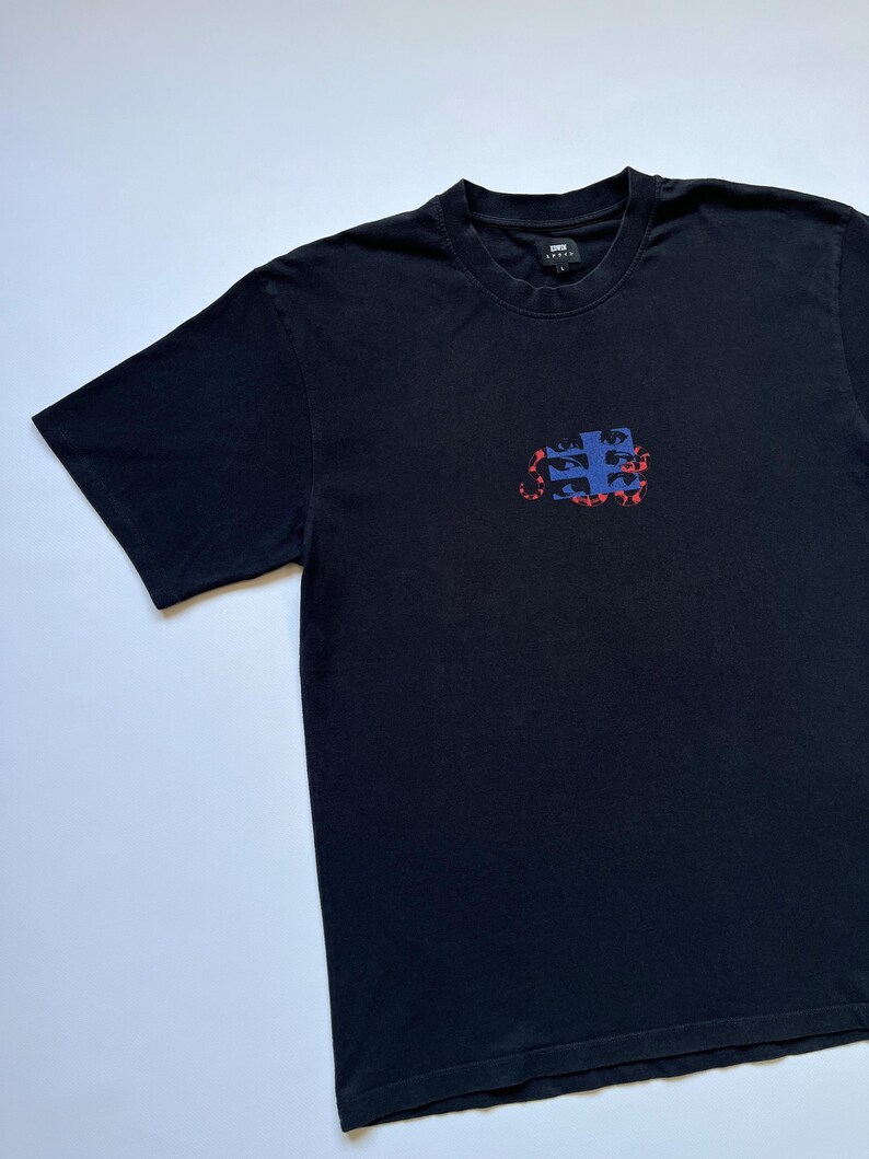 K&ouml;nnte beinhalten: Schwarzes T-Shirt mit kurzen &Auml;rmeln und Rundhalsausschnitt. Das Shirt hat einen rechteckigen Aufdruck auf der Vorderseite mit blauen und roten abstrakten Formen. Aus weichem Material, geeignet f&uuml;r den l&auml;ssigen Gebrauch.