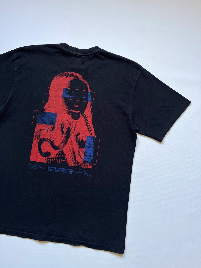 K&ouml;nnte beinhalten: Schwarzes T-Shirt mit einer rot-blauen Grafik eines menschlichen Gesichts und abstrakten Formen. Die Grafik enth&auml;lt den wei&szlig;en Text "SECOND PRINCESS". Das T-Shirt ist aus weichem Material.