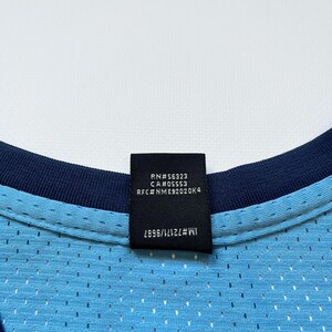 May include: Close-up of a light blue mesh jersey with a navy blue collar. A black tag displays text including "RN#56323" and "CA#05553". The jersey has a perforated design.
