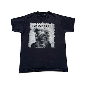 May include: Black Stonesour t-shirt featuring a distressed graphic of a person's face with the band's name above. The design is in shades of gray and white. The shirt is a crew neck style.