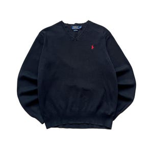May include: A navy blue long-sleeve V-neck sweater featuring a red embroidered Polo Ralph Lauren logo on the left chest. The garment has a ribbed neckline, cuffs, and hem, with a blue and white brand label stitched inside the collar area.