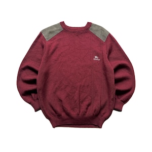 May include: A long-sleeve crewneck jumper in a deep burgundy colour featuring grey suede-like shoulder patches. The garment has a ribbed collar, cuffs, and hem, with a small embroidered logo on the left chest that reads Burberrys.