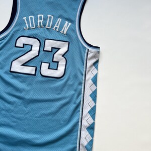 May include: Light blue basketball jersey with the name "JORDAN" and the number "23" in white. The jersey has a mesh design and a white and blue diamond pattern on the side.