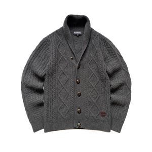 May include: A dark grey cable-knit cardigan with a shawl collar and button fastening. The sweater has a diamond pattern and a small leather patch. The brand name "Barbour" is visible on the collar.