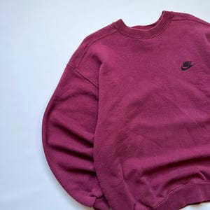 Puede incluir: Una sudadera Nike granate con cuello redondo y mangas largas. El logotipo de Nike est&aacute; bordado en negro en la parte superior izquierda del pecho. La sudadera est&aacute; hecha de un material suave y c&oacute;modo.