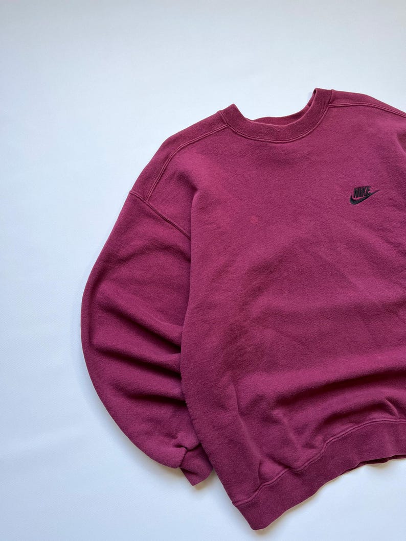 Puede incluir: Una sudadera Nike granate con cuello redondo y mangas largas. El logotipo de Nike est&aacute; bordado en negro en la parte superior izquierda del pecho. La sudadera est&aacute; hecha de un material suave y c&oacute;modo.