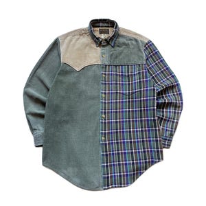 Può includere: Una camicia a maniche lunghe con bottoni e design a blocchi di colore. Il lato sinistro è in velluto a coste verde salvia, mentre il lato destro e le maniche presentano un motivo a quadri verde, blu e bianco. Include un carré in velluto beige.
