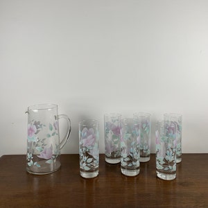 Puede incluir: Un juego de siete vasos de beber de vidrio transparente con un diseño floral. Los vasos tienen un patrón floral rosa y azul con hojas verdes. El juego incluye una jarra con el mismo diseño floral.