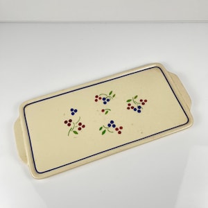 Peut inclure: Plateau de service rectangulaire en céramique crème avec une bordure et des poignées bleues. Le plateau est décoré de grappes de baies rouges et bleues avec des feuilles vertes. Une pièce décorative pour servir des aliments.