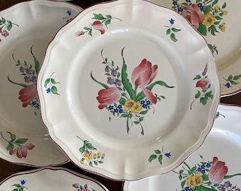May include: A set of cream-colored ceramic plates with scalloped edges and a thin maroon rim. Each plate features a central floral motif with pink tulips, yellow blossoms, purple sprigs, and green leaves, with smaller floral accents on the rims.