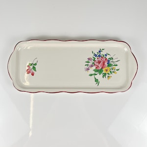 Puede incluir: Una bandeja de servicio rectangular de cerámica con borde festoneado y un fino borde rojo. La superficie de color blanco roto presenta un gran ramo de flores de colores en el lado derecho y un pequeño capullo de flor roja a la izquierda.