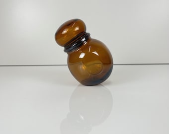 May include: A small, amber-colored glass bottle with a rounded body and a bulbous top. The bottle has a dark brown neck and a smooth, reflective surface. The design is simple and elegant, suitable for perfumes or essential oils.