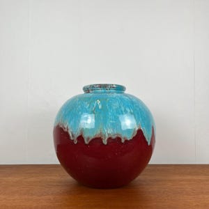 Könnte beinhalten: Eine runde Keramikvase mit blauer und roter Glasur. Die obere Hälfte der Vase ist hellblau mit Marmoreffekt, die untere Hälfte ist tiefrot.