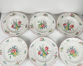 May include: A set of six white ceramic plates with scalloped edges, each featuring a hand-painted floral bouquet in the center with red, pink, yellow, and blue flowers, accented by green leaves and small floral motifs along the outer rim.