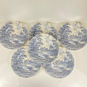 Peut inclure: Six assiettes en céramique bleues et blanches avec un motif de paysage. Chaque assiette présente une illustration détaillée d'arbres, de bâtiments et d'un plan d'eau. Les assiettes sont disposées en cercle.