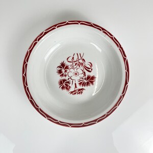 May include: A white ceramic bowl with a red floral design in the center and a red scalloped border. The bowl has a simple, elegant design, perfect for serving soups, salads, or desserts. The bowl is a classic piece of kitchenware.