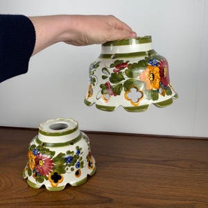 Op de afbeelding: Twee witte keramische bloempotten met groene en witte gegolfde randen. De potten zijn versierd met handgeschilderde bloemenontwerpen in tinten rood, geel, oranje, groen en blauw.