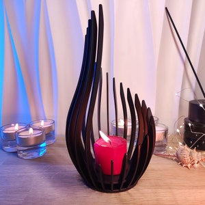 May include: Black metal candle holder shaped like a flame with a red candle inside. The holder is surrounded by four small glass candle holders with white candles.