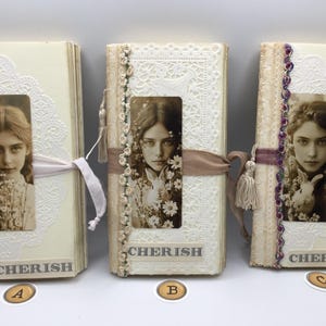 May include: Three vintage-style journals with cream-colored covers and decorative lace and ribbon accents. Each journal features a sepia-toned portrait of a young woman and the word "CHERISH" at the bottom. The journals are tied with ribbons.