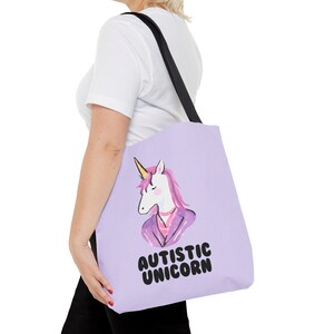 Può includere: Una borsa tote viola con un unicorno bianco che indossa una giacca viola e il testo "Autistic Unicorn".