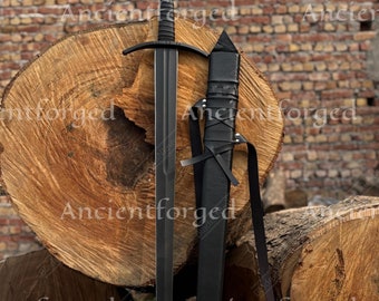May include: A black medieval sword with a leather scabbard. The sword is resting on a pile of wooden logs.
