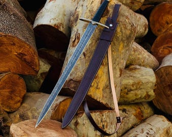 May include: A silver sword with a black leather scabbard and a brown leather strap. The sword is resting on a pile of logs.