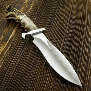 May include: A hunting knife with a brown antler handle and a silver blade. The knife is lying on a wooden surface.