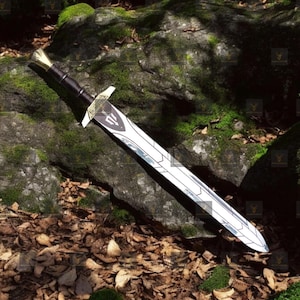 May include: A silver sword with a black handle and gold accents lies on a bed of brown leaves and moss covered rocks. The sword has a decorative design on the blade.