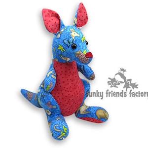 May include: A stuffed kangaroo toy with a blue patterned body and red accents. The kangaroo has a red belly, ears, and nose. The blue fabric features a pattern of animals and floral designs. The toy is sitting upright.