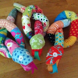 May include: Three colorful patchwork fabric snakes with different patterns and colors. The snakes are knotted together and have a playful, whimsical design.