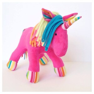 May include: A pink plush unicorn toy with a rainbow striped horn and a blue and yellow mane. The unicorn has rainbow striped legs and hooves.