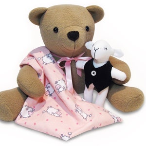 May include: A brown teddy bear wearing a pink blanket with a white sheep pattern and holding a white lamb wearing a black vest.