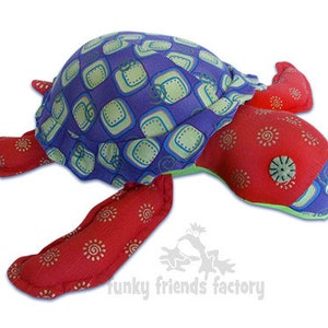 Op de afbeelding: Een handgemaakt pluche schildpad speelgoed met een paarse en groene gepatroneerde schil, een rood stoffen lichaam en gouden accenten. Het speelgoed heeft een knoop oog en is gemaakt door "Funky Friends Factory".