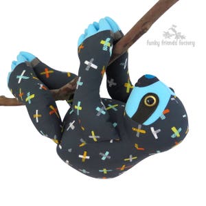 Peut inclure: Un jouet en peluche de paresseux bleu et gris avec un motif de signe plus noir et blanc suspendu à une branche. Le jouet a un visage bleu avec un cache-œil noir et un œil bouton noir.