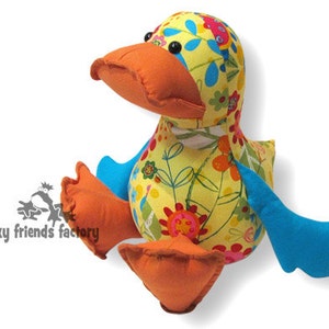 May include: A colourful plush duck toy with a yellow body, orange beak, blue wings, and a floral pattern. The duck is sitting on its feet with its wings spread out.