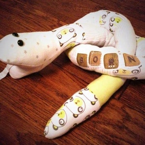 May include: A white and yellow fabric snake toy with black eyes and the word "BORN" spelled out on the body.