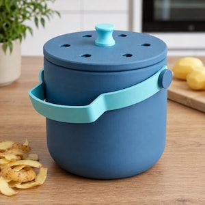 May include: A cylindrical dark blue storage bin with a light blue handle and a matching lid featuring ventilation holes and a central light blue knob. The container has a smooth matte finish and is designed for storing vegetables in a kitchen setting.