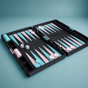 May include: A black backgammon board featuring alternating light pink and turquoise triangular points. The set includes matching pink and turquoise circular checkers stacked in side compartments and two white six-sided dice with black pips.