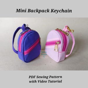 May include: Two miniature backpack keychains. One is purple with a pink zip, and the other is light pink with a pink zip. Both have small handles and gold-coloured hardware. The text "Mini Backpack Keychain" and "PDF Sewing Pattern with Video Tutorial" are displayed.