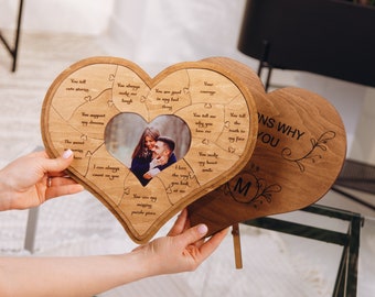Pode incluir: Um quebra-cabeça de madeira em forma de coração com uma moldura de foto no centro. As peças do quebra-cabeça têm mensagens gravadas sobre o amor, como "Você me faz rir" e "Você conta histórias fofas". O verso do quebra-cabeça tem as palavras "Razões pelas quais eu te amo" e um design floral.