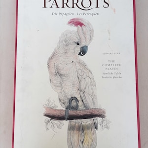 May include: A book cover titled "THE PARROTS" with text in multiple languages. It features a detailed illustration of a white cockatoo perched on a branch. The book is by Edward Lear and published by Taschen.