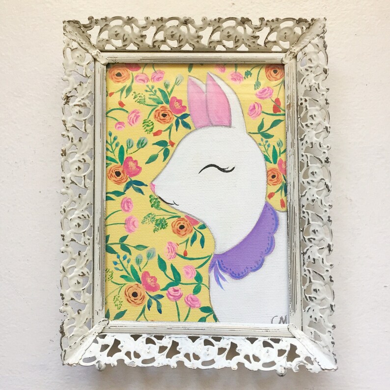 May include: A white rabbit with closed eyes and a purple collar is painted on a yellow background with pink and orange flowers. The painting is framed in a white ornate frame.