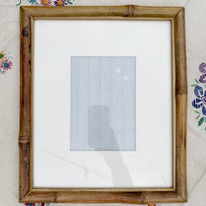 Puede incluir: Un marco de fotos rectangular de bambú con un paspartú blanco. El marco es de color marrón claro y tiene un aspecto natural y texturizado. La abertura del paspartú es rectangular. El marco está vacío.