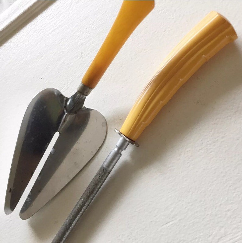 May include: A set of two vintage kitchen tools with yellow plastic handles. The first tool is a cake server with a heart-shaped blade. The second tool is a knife with a serrated blade.